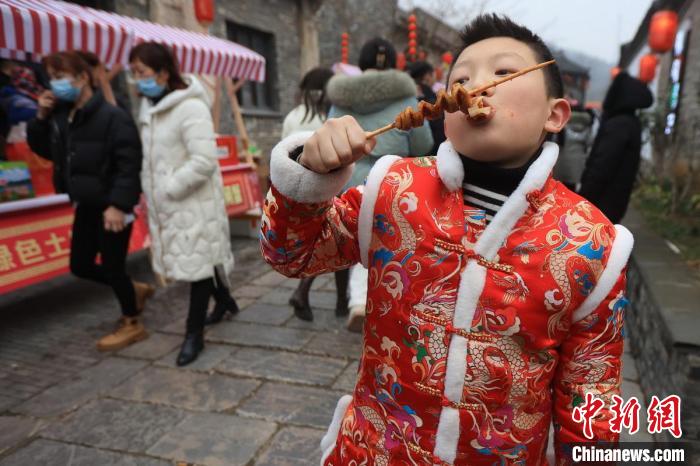 身着喜庆服装的男孩品尝美食。　泱波 摄